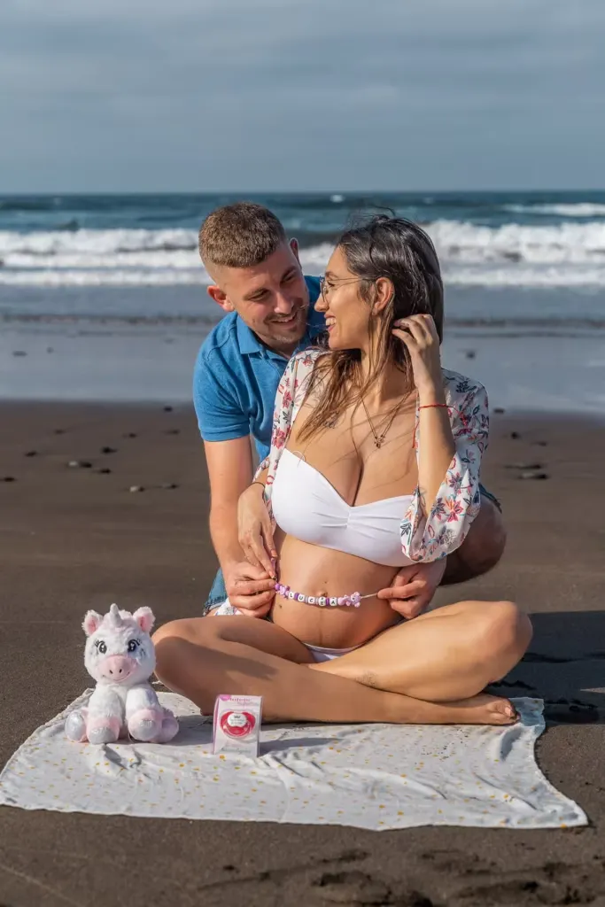 Werdendes Paar sitzt am Strand von Playa del Inglés mit persönlichen Baby-Accessoires