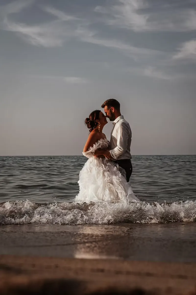 Bride in flowing white dress walking barefoot through the shallow water