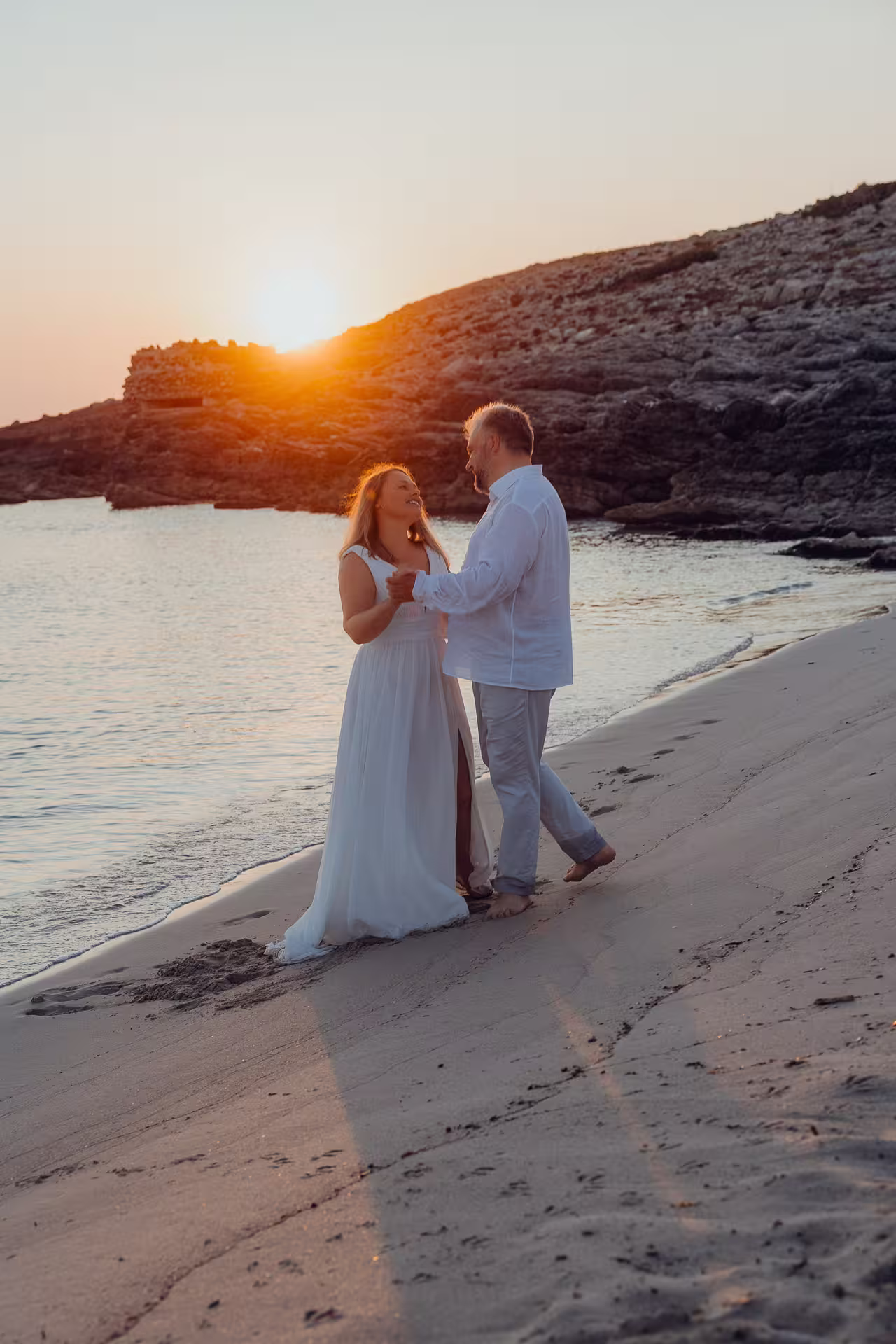 Lachendes Brautpaar hält Händchen beim romantischen Sonnenaufgang am Sandstrand