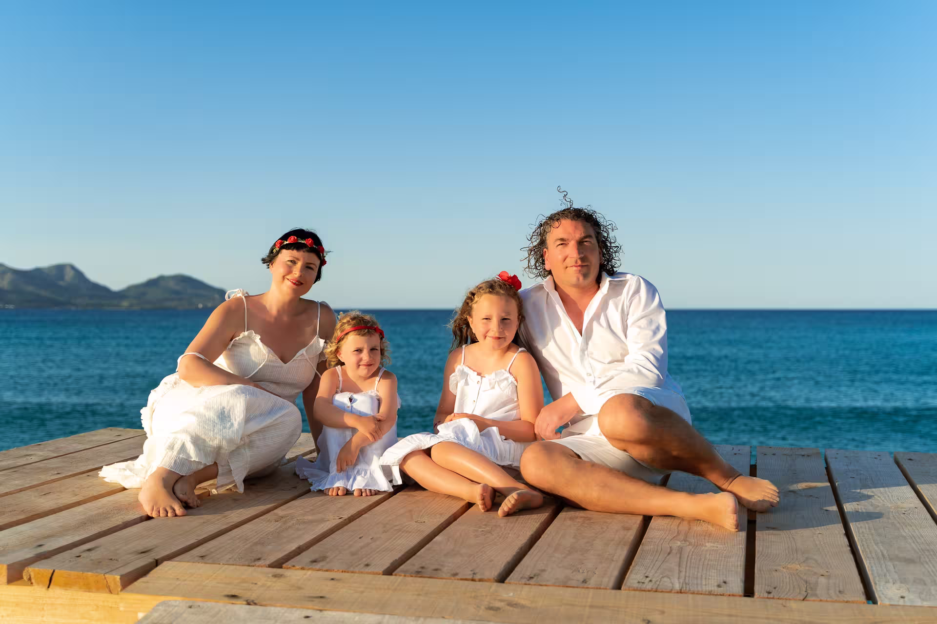 Family with 2 children sitting on the wooden pier in Alcudia