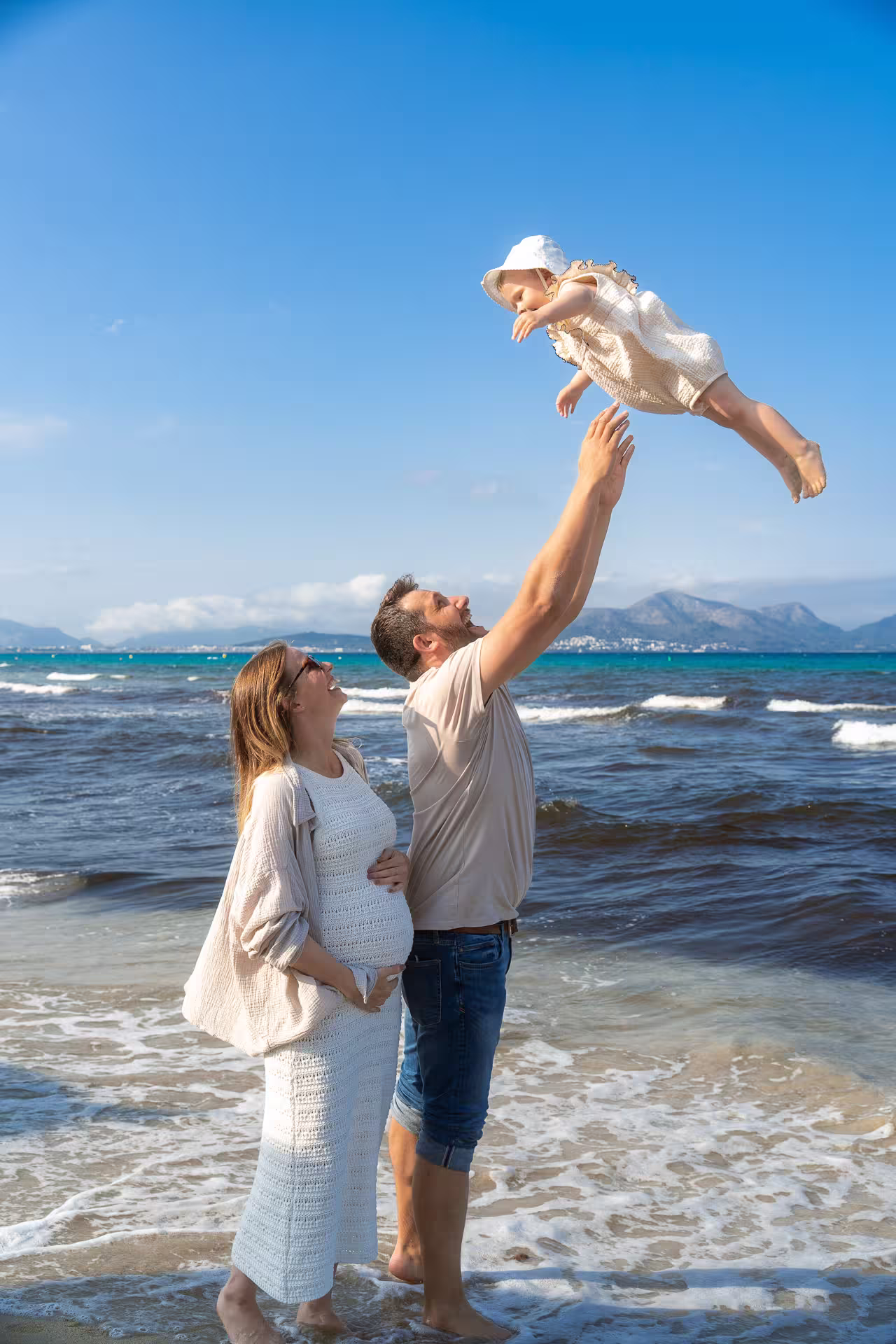 Young family by the sea and father tossing his little daughter in the air