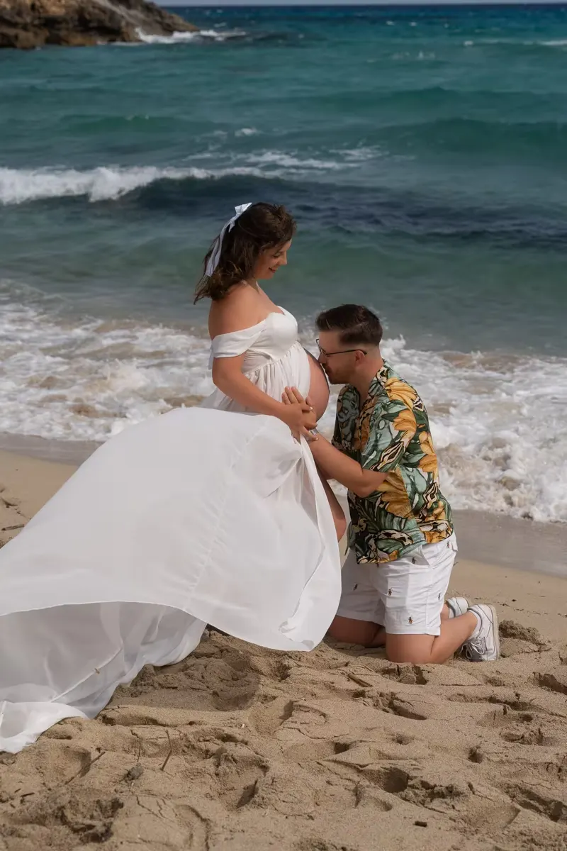 Couple gazing out to sea from a cliff top, holding hands over the pregnant belly