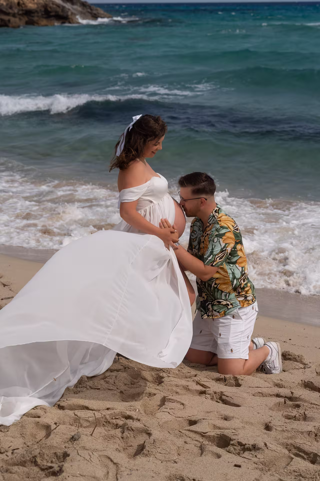 Couple gazing out to sea from a cliff top, holding hands over the pregnant belly
