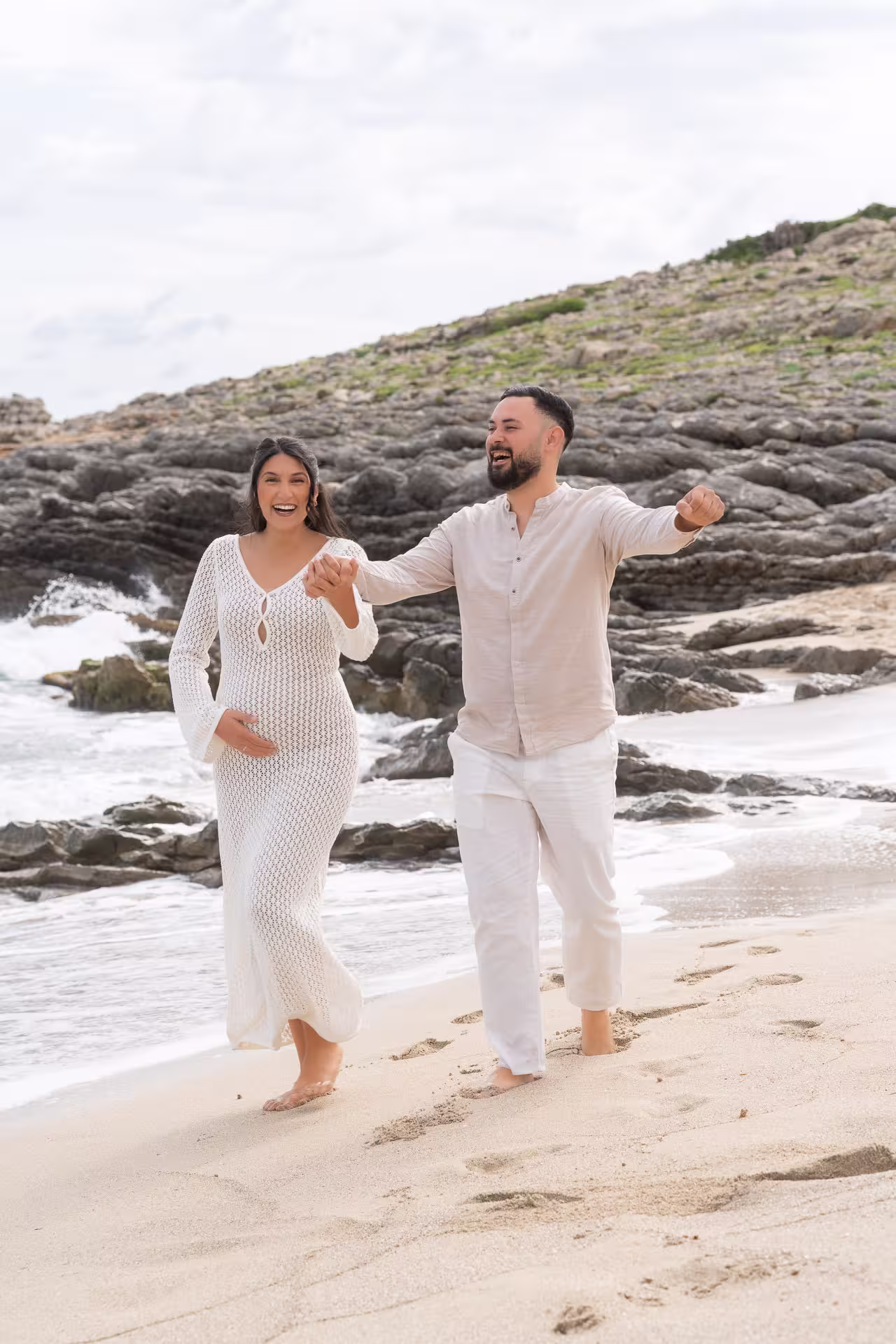 Pregnant woman cradling her baby bump on the beach at golden hour in Mallorca