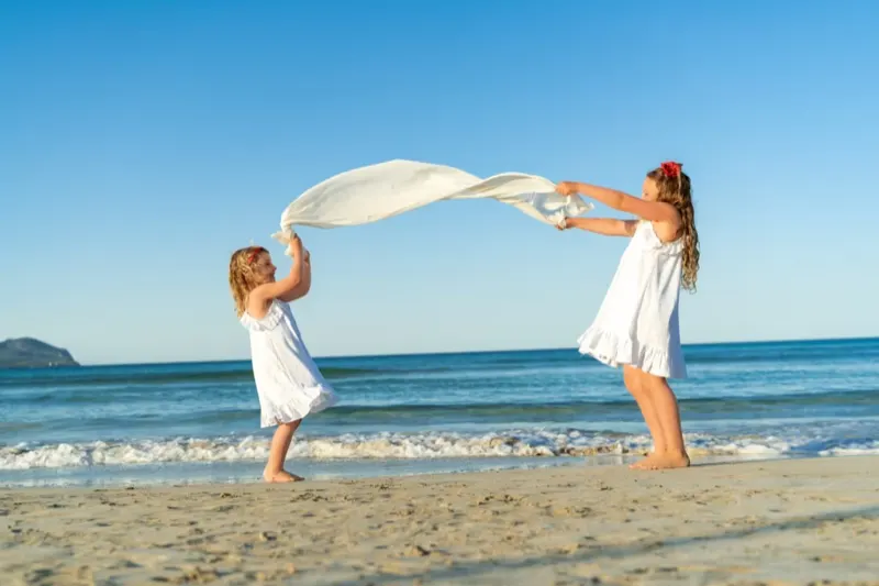 2 Kinder schwenken ein Tuch am Strand von Cala Millor