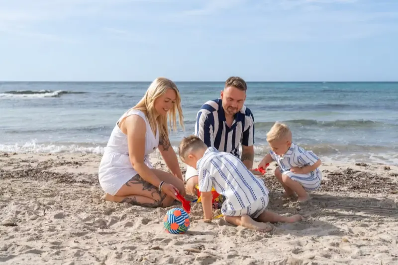Familie mit 2 Kindern sitzen im Sand am Meer von Cala Millor