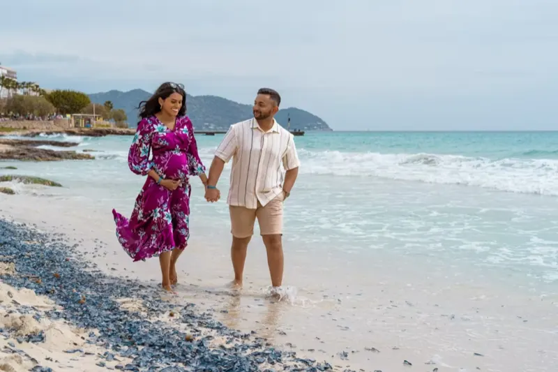 Junges Paar läuft am Strand von Cala Millor und bewundert den Babybauch