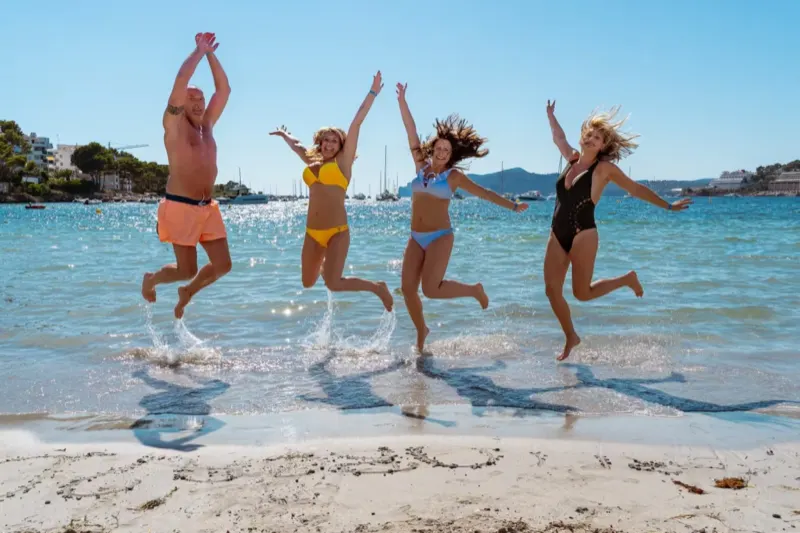 Eine Gruppe Freunde springt fröhlich gemeinsam ins Meer am Strand