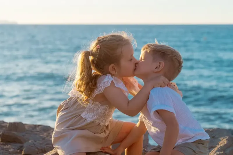 Geschwister – kleines Mädchen und Junge küssen sich beim Sonnenuntergang am Meer