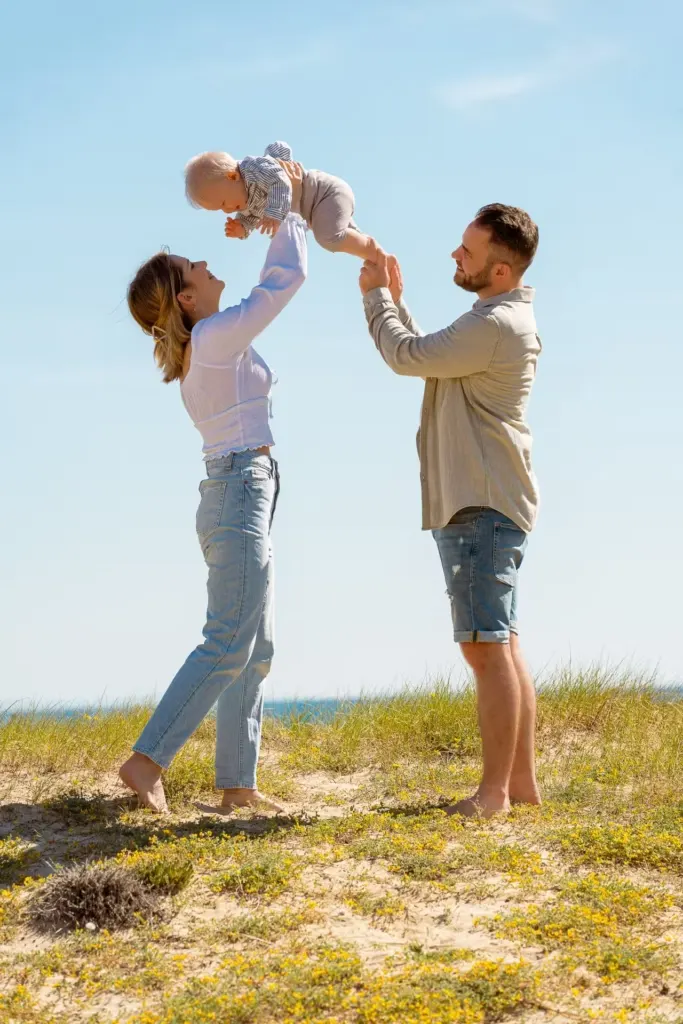 Junge Eltern heben ihr Baby hoch in den blauen Himmel in einer Dünenlandschaft
