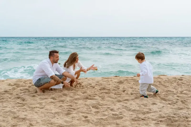 Kleiner Junge rennt mit offenen Armen auf seine Eltern am Strand zu