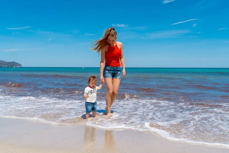 Mutter läuft Hand in Hand mit ihrem Sohn durch flaches Wasser am Strand
