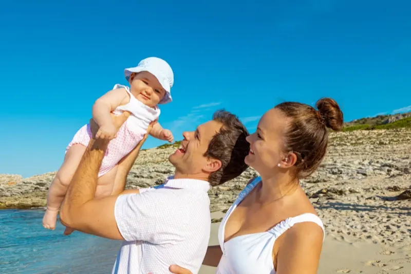 Stolzer Vater hebt sein lachendes Baby in die Luft am Strand von Mallorca