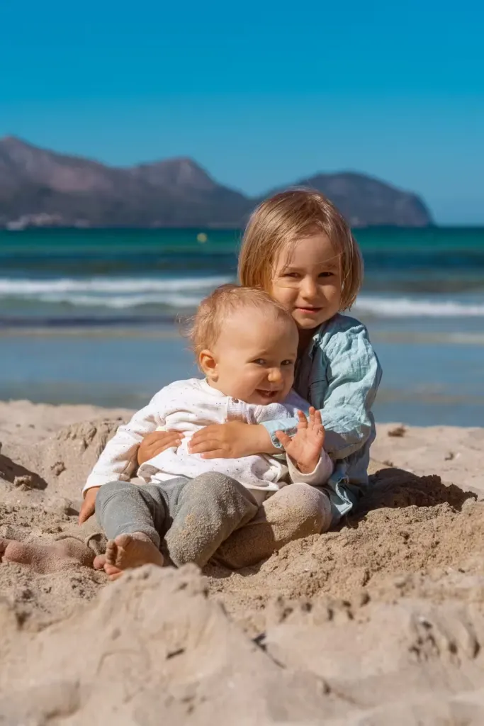 Zwei kleine Geschwister umarmen sich liebevoll im Sand am Mallorca Strand