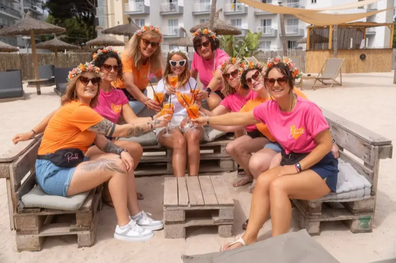 Eine fröhliche Gruppe stößt bei Strandparty mit Cocktails an beim JGA Mallorca