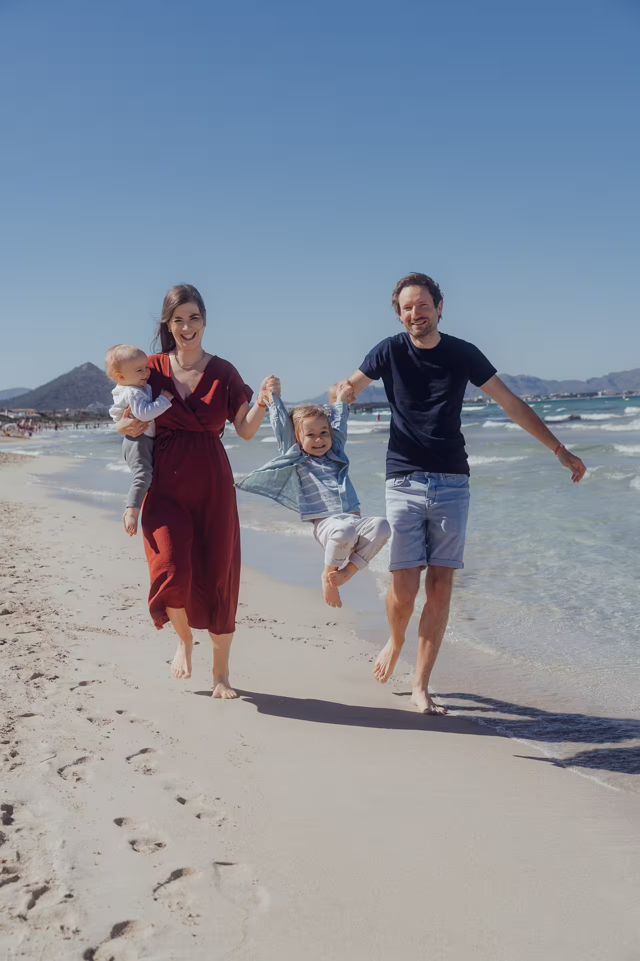 Happy family with two children being lifted by their hands on the sandy beach