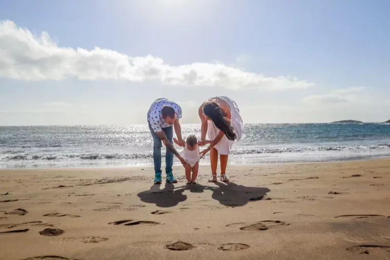 Eltern helfen ihrem Baby bei den ersten Schritten am Strand von Gran Canaria