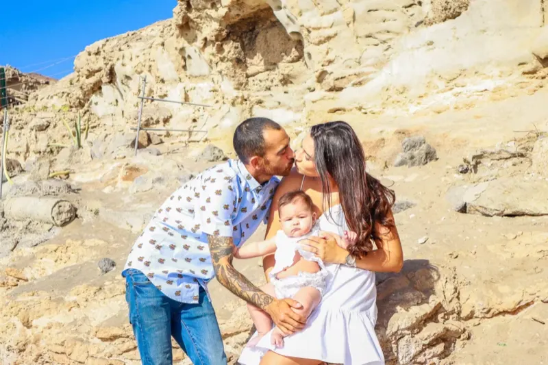 Eltern küssen sich liebevoll während sie ihr Baby halten – Familienshooting Gran Canaria