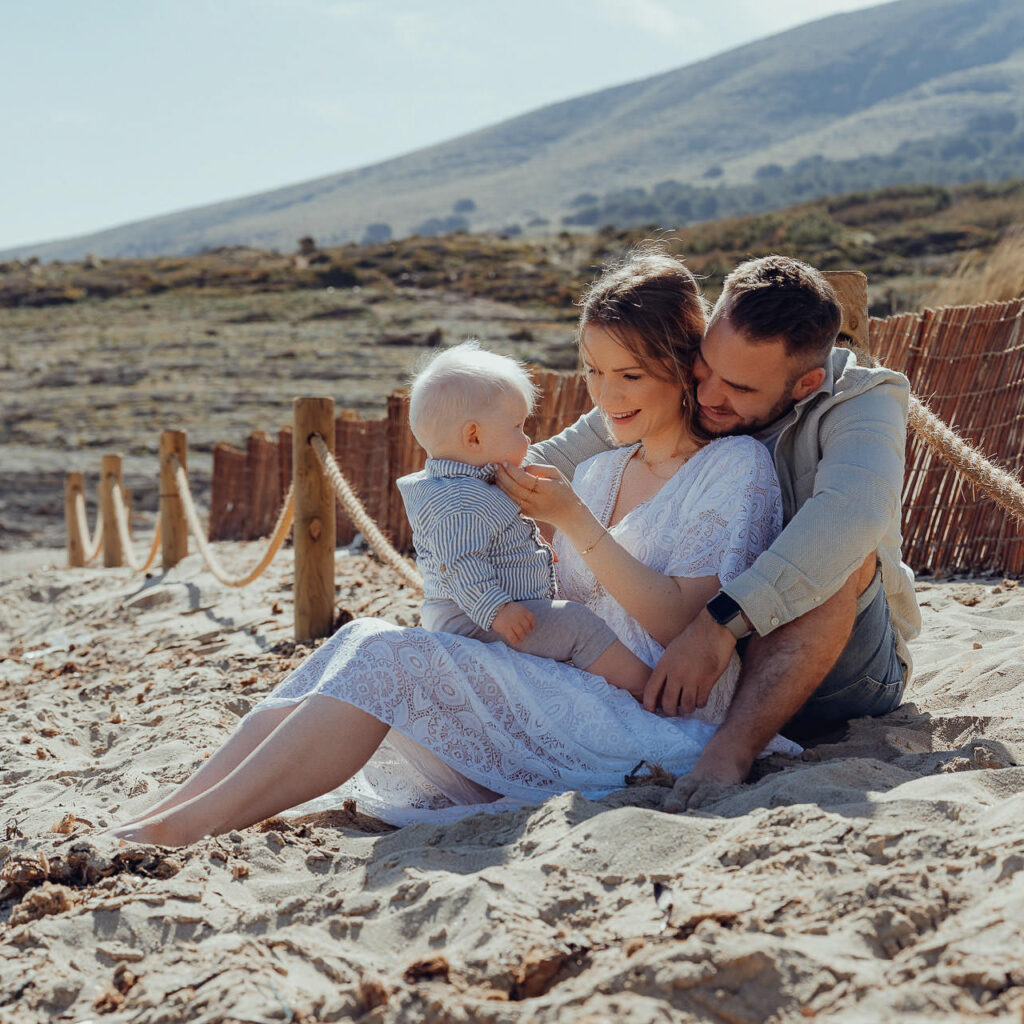 Junge Familie mit Baby sitzt im Samd am Meer