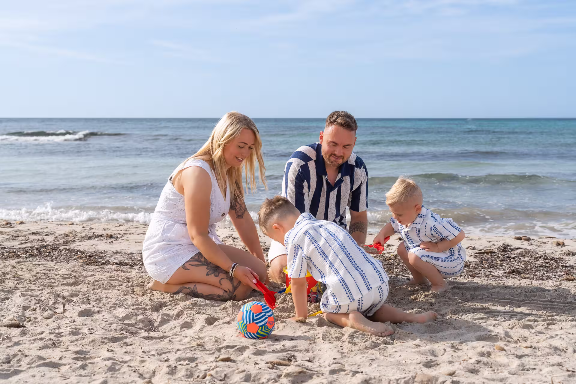 Familie mit 2 Kindern sitzen im sand am Meer und spielen.