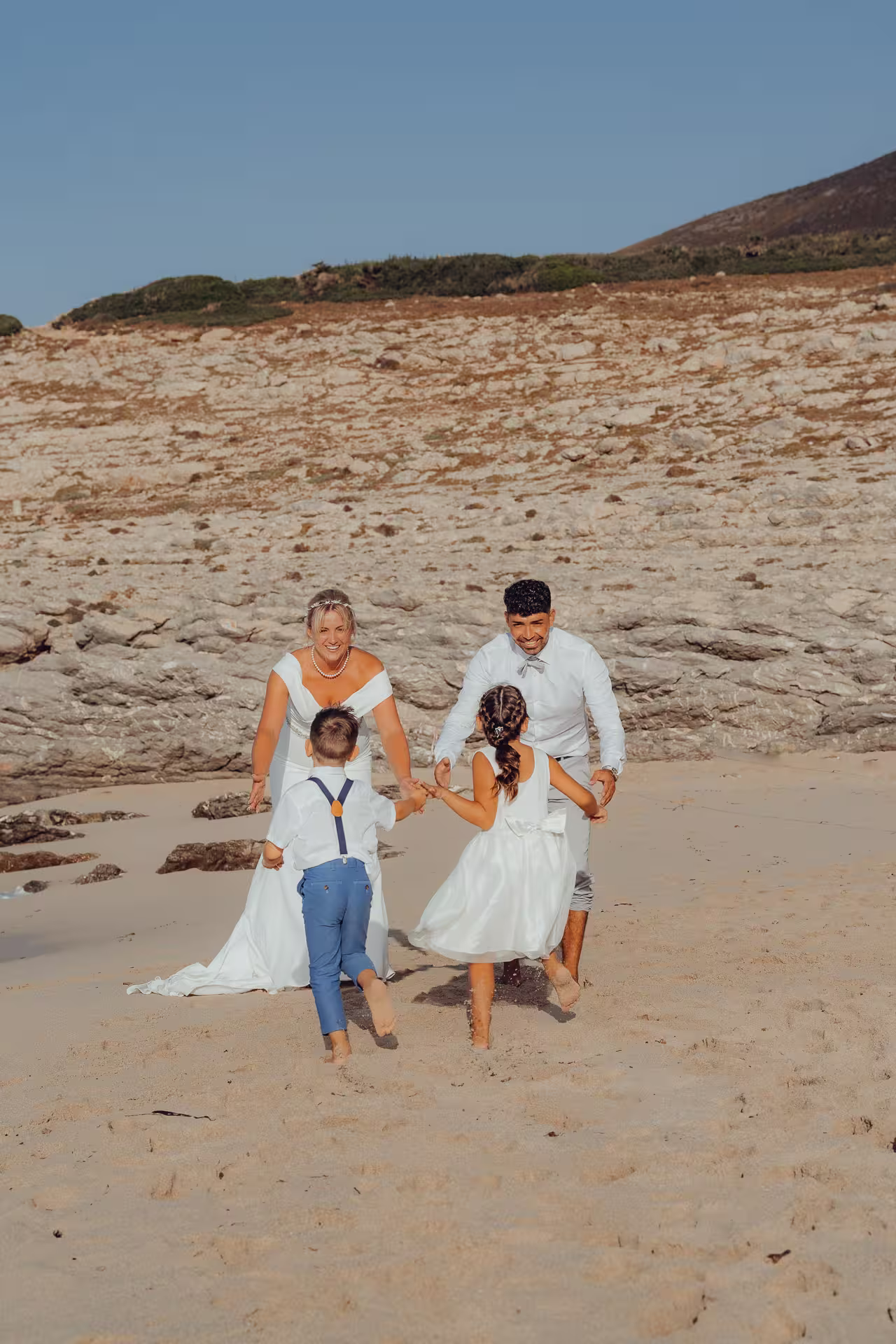 Fotoshooting After Wedding Mallorca: Ein Brautpaar feiert mit seinen beiden Kindern und läuft lachend über den Sandstrand.