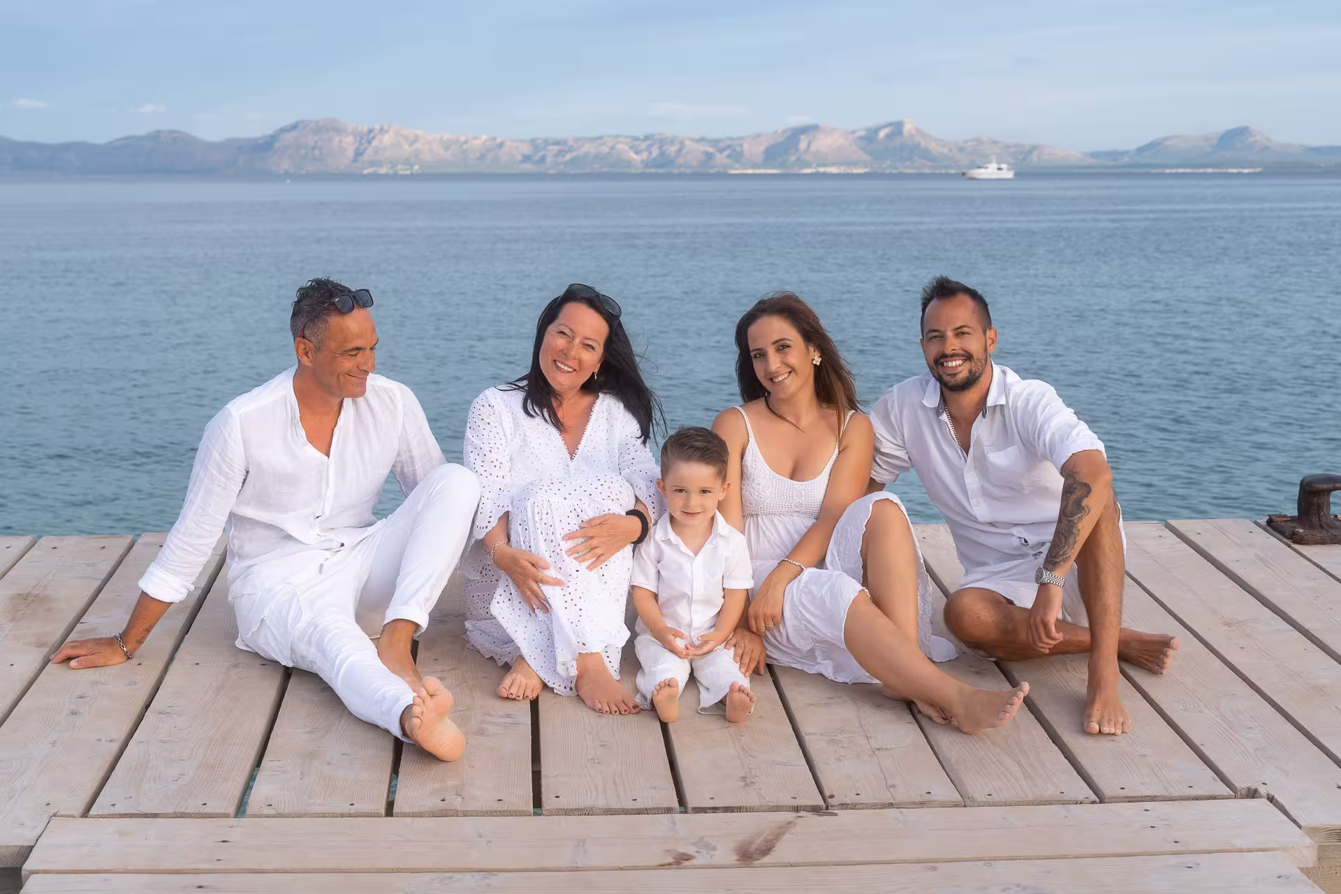 Familie sitzt fröhlich auf dem Holzsteg in Alcudia