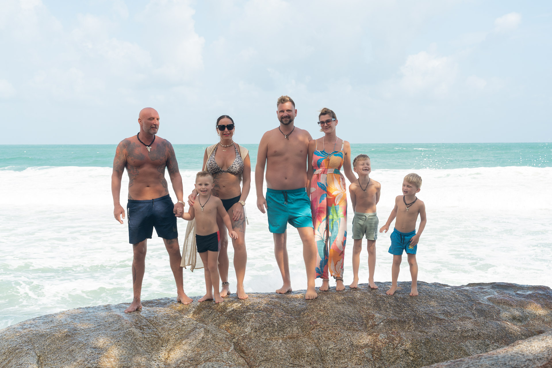 Gruppen Fotoshooting in Thailand – zwei Familien am Strand mit Wellen im Hintergrund, professionell aufgenommen vom Thailand Fotograf.
